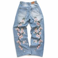 Jean en denim bleu pâle délavé avec broderie florale rose enveloppante, poches arrière et empiècement en cuir neutre