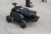 Châssis de robot tout-terrain compact noir avec capteur de vision, reposeur sur une herbe verte fraîche pour les tests de conduite