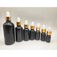 Flacon compte-gouttes cylindrique en verre noir mat personnalisé avec logo, bouchon doré/noir, pour huiles essentielles, sérums et cosmétiques – Vente en gros