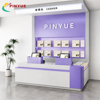 Comptoir de caisse moderne violet et blanc avec étagères de présentation multi-niveaux, affiche rétroéclairée et deux postes de point de vente pour les magasins de cadeaux