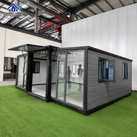 Maison conteneur moderne extensible en acier avec auvent en verre, bardage imitation pierre, fenêtres à battants à cadre noir, entrepôt entièrement meublé