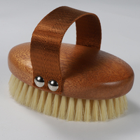 Cepillo exfoliante ovalado de madera de acacia con cerdas de jabalí, correa de mano de lona blanca y remaches plateados para un agarre seguro en superficies húmedas.