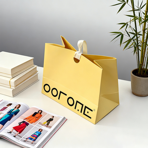 حقيبة ورقية صفراء زاهية بخط أسود جريء، تتميز بمقابض بيضاء متينة، تم التقاطها في نمط حياة بسيط - Product Image 3