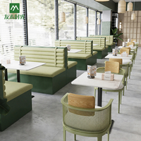 Banquette de restaurant moderne et commerciale, avec sièges carrés, revêtement vert, table à manger en marbre et chaises à dossier en rotin.