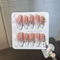 Faux ongles en acrylique rose nude effet œil de chat avec bouts français transparents, fleurs blanches et accents de strass pour un style minimaliste et nuptial