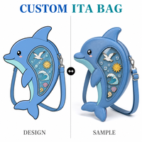 Sac bandoulière Ita motif Dauphin mignon, en cuir PU texturé bleu clair, avec visage Chibi et joues rosées, forme croissant, fenêtre transparente et motifs océaniques