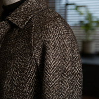 Manteau en laine 100% pour homme, gris anthracite, à chevrons, col tailleur, simple boutonnage, texture tissée grossière, mettant en valeur l'esthétique hivernale