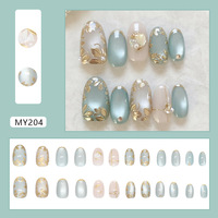 Ongles courts ovales minimalistes style Instagram, motif œil de chat vert raisin, fleur dorée 3D, paillettes, strass et fragments de perles