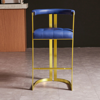 Tabouret de bar en acier inoxydable doré avec siège capitonné bleu marine, dossier enveloppant et base courbée, repose-pieds inclus
