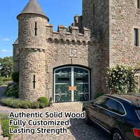 Porte de garage haut de gamme sur mesure en bois massif, style gothique cintrée, avec ferronnerie décorative en fer forgé et petits fenêtres trempées, pour château et manoir