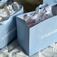 Sac cadeau en papier bleu poussière mat avec ruban en satin blanc et poignée à nœud, logo personnalisé en serif, sac de luxe pour boutique de parfums