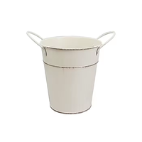 Pot tanaman vintage bergaya farmhouse, terbuat dari logam putih antik dengan tepi yang terurai, bentuk meruncing, dan dua pegangan samping.