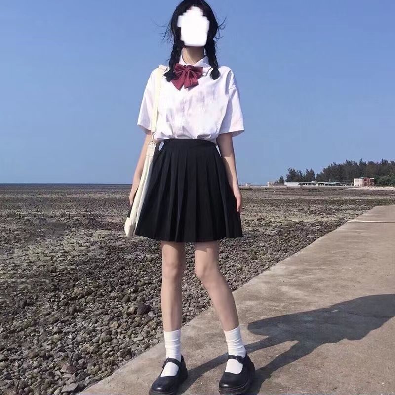 Chemise blanche à manches courtes, mini-jupe noire et nœud papillon rouge.