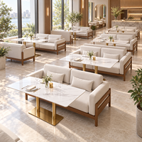 Ensemble de canapés de restaurant de style côtier moderne, chaises et tables, canapé en chêne clair avec coussins crème et table en marbre blanc avec pieds dorés