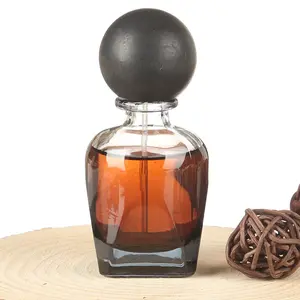 MS2010 # Parfum ambre foncé dans une bouteille en verre avec capuchon sphérique noir et décoration boule tissée sur une surface en bois