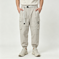 Pantalon cargo beige pour homme, coupe fuselée, avec ceinture à boucle en sangle, poignets élastiqués, poches cargo à rabat, poches zippées, empiècements aux genoux, style utilitaire