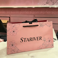 Sac en papier personnalisé imprimé rose clair avec laminage brillant, poignées en corde noire et doublure intérieure rouge pour l'emballage de vêtements féminins