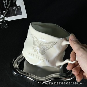 Taza de cerámica con diseño de mariposa, color blanco lechoso y plateado, con platillo para té, café y otras bebidas. - Product Image 1