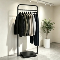 Porte-vêtements moderne minimaliste en métal noir avec cadre à coins arrondis et base lourde centralisée pour boutique de créateurs