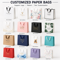 Sac en papier cadeau blanc de luxe recyclable en gros d'usine avec nœud en ruban noir et logo personnalisé pour l'emballage de vêtements et d'artisanat de détail