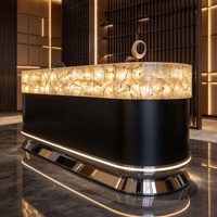 Comptoir de réception en pierre naturelle rétroéclairée, quartz blanc cristallin, translucide et lumineux, avec base noire mate et finition métallique.