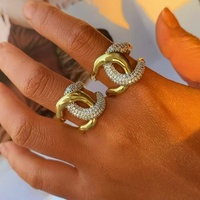 Cincin perhiasan statement chunky untuk wanita, dengan desain band emas melengkung yang saling menyatu dan band kristal pave.