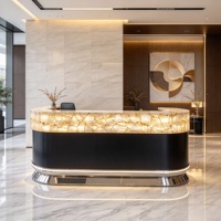 Comptoir de réception en pierre naturelle rétroéclairée, quartz blanc cristallin, translucide et lumineux, avec base noire mate et finition métallique.