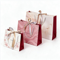 Sac shopping en papier marbré rose avec logo personnalisé, décoration nœud en satin et poignée torsadée en corde pour emballage cadeau de boutique cosmétique