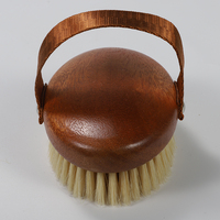 Cepillo exfoliante ovalado de madera de acacia con cerdas de jabalí, correa de mano de lona blanca y remaches plateados para un agarre seguro en superficies húmedas.