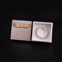 Boîte à bijoux de luxe en papier rigide carré, couleur or champagne, avec ruban et logo personnalisé, pour la présentation de bracelets.