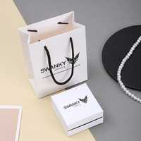 Ensemble sac en papier blanc A1 et boîte à bijoux avec poignées noires, base blanche, intérieur foncé, étui carré et présentoir de vente au détail