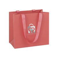 Sac spécial en lin rose à texture grainée, aspect de qualité cadeau, avec poignée en ruban estampé argenté, prêt pour les comptoirs de boutiques.