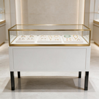 Vitrine de présentation de bijoux de luxe en verre trempé avec cadre doré, socle blanc, pieds carrés noirs et comptoir multi-plateaux