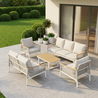 Ensemble de salon d'extérieur moderne en métal blanc, sièges à texture tressée, tables rondes avec accents en bois et coussins gris moelleux, idéal pour le patio