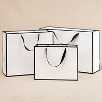 Sacs cadeaux blancs à bordure noire en stock, sacs fourre-tout personnalisés pour vêtements avec logo publicitaire imprimé, sacs en carton blanc