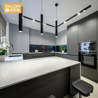 Meubles de cuisine BALOM blancs sans poignées, îlot avec comptoir en quartz et bar à petit-déjeuner, style moderne et minimaliste.