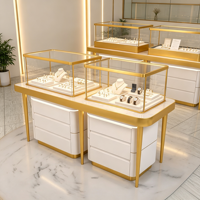 Comptoir de présentation de bijoux compact et combiné, vitrine en verre à cadre fin doré avec base de rangement à tiroirs blancs et plateforme ronde en marbre