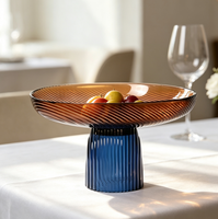 Twee-kleurige glazen fruitschaal, amberkleurige plaat met blauwe geribbelde voet, moderne decoratieve serveerschaal op voet voor thuis op tafel.