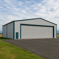 Hangar d'avion gris avec porte coulissante pleine largeur, entrée latérale pour le personnel, espace d'accueil pavé et accès à l'aérodrome