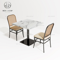 Ensemble de mobilier de café-restaurant : table carrée en marbre blanc, pieds noirs, chaises avec dossier tressé et coussin beige pour salle à manger de café