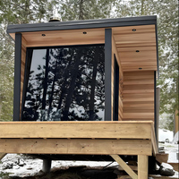 Sauna extérieur moderne en bois foncé avec paroi en verre |   Sauna parfait intégré au jardin pour le bien-être et la relaxation dans la cour