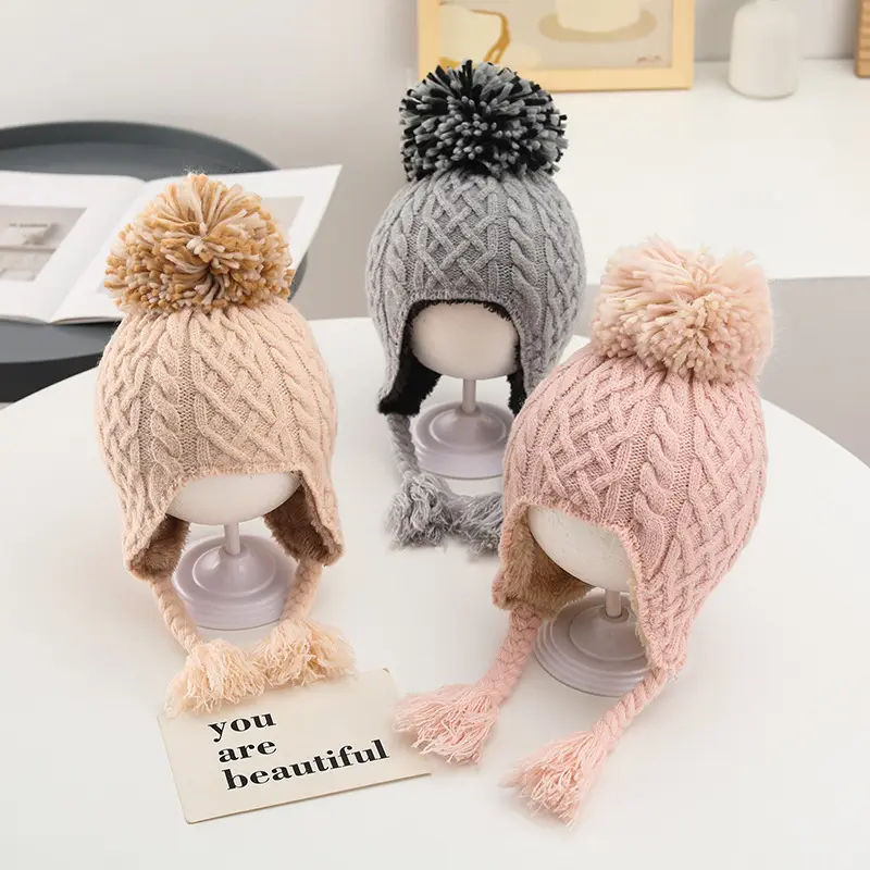 Bonnets de protection des oreilles doublés en polaire pour bébé, doux et chaud, d'hiver à la mode en gros Chapeau tricoté de couleur unie et mignon avec des boules de poils Chapeau tressé