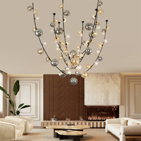 Lustre décoratif en forme d'arbre artistique à branches, avec globes en verre de tailles variées et structure en métal noir, idéal pour hall à plafond haut