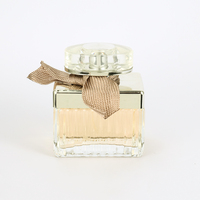 Perfume Femenino en Envase Rectangular de Vidrio con Franjas Plateadas, Lazo de Cinta Marrón, Tapa Dorada y Caja Dorada. Aroma Atemporal para Aniversario.