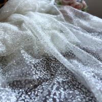 Tissu blanc opaque et scintillant avec des paillettes dorées, idéal pour les séances photo de robes de mariée et de soirée.