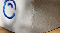 Un chapeau de sauna en pure laine crème qui capte la lumière du matin et présente une seule courbe bleue comme une signature discrète