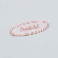Patch brodé ovale avec bordure, fond blanc et caractères roses, adhésif thermofusible au dos, design minimaliste
