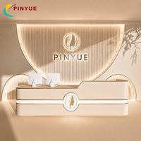 Comptoir de réception personnalisé en crème pour bureau, avec bordure dorée, comptoir incurvé à niveaux, logo semi-circulaire rétroéclairé par LED, salon de beauté