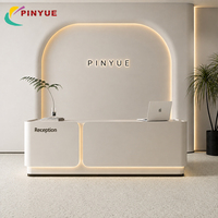Comptoir de réception moderne crème avec comptoir arrondi, éclairage LED halo chaud, mur arqué, design minimaliste et affichage haut de gamme pour hall d'accueil