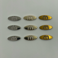 Étiquettes métalliques personnalisées ovales en strass anti-corrosion avec logo lettre M, vente en gros pour vêtements, sous-vêtements, sacs, casquettes